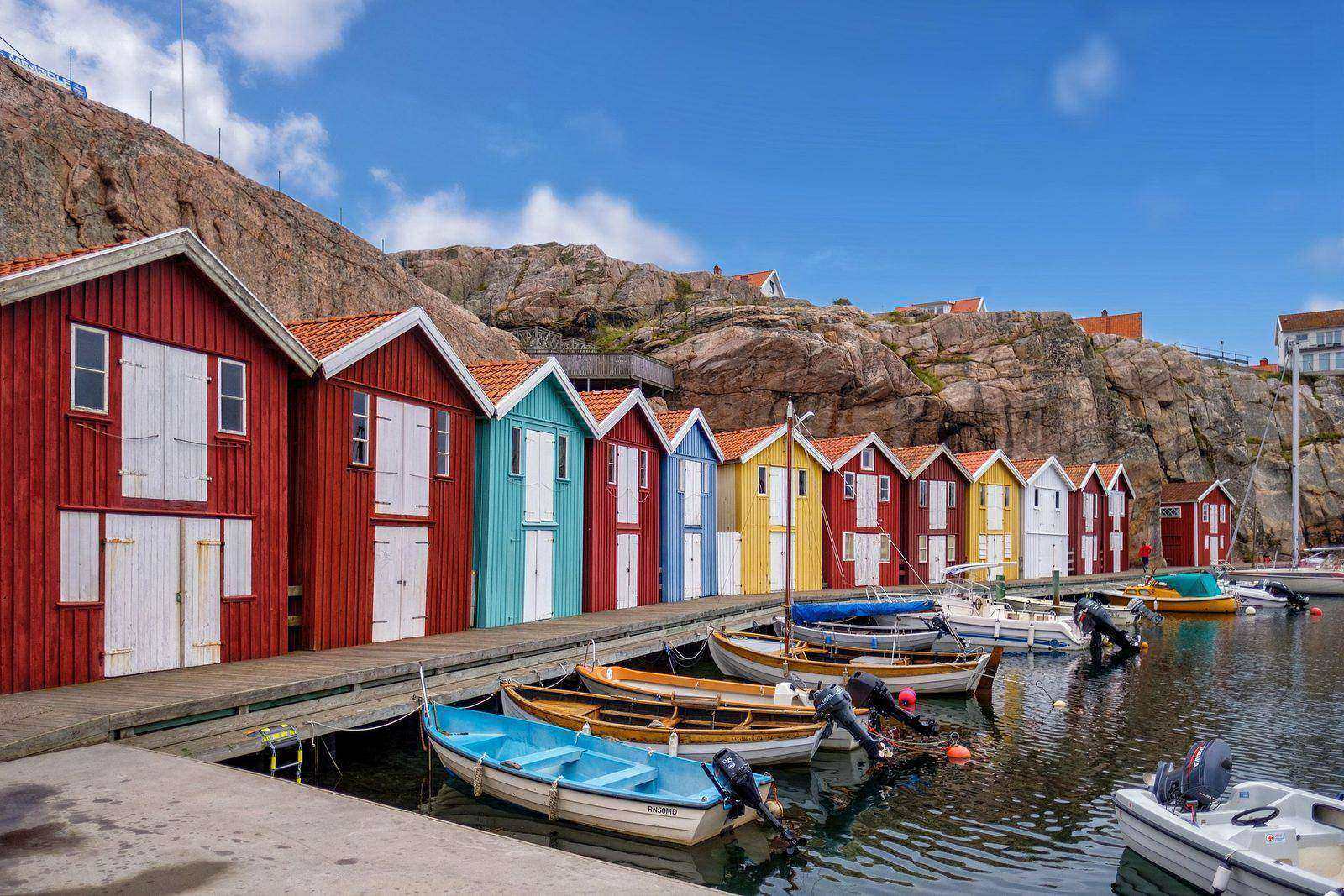 Färgglada sjöbodar och småbåtar i en hamn på västkusten